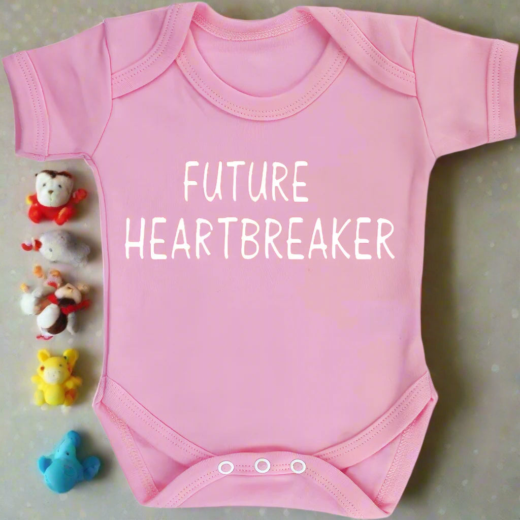 Pink baby onesie with 'FUTURE HEARTBREAKER' text on a white background