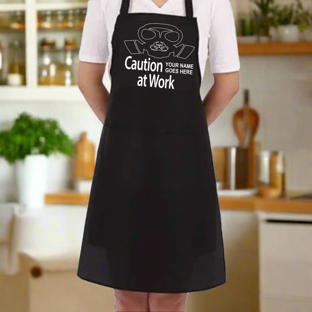 Black apron with 'Caution at Work' text and customizable name on a white background