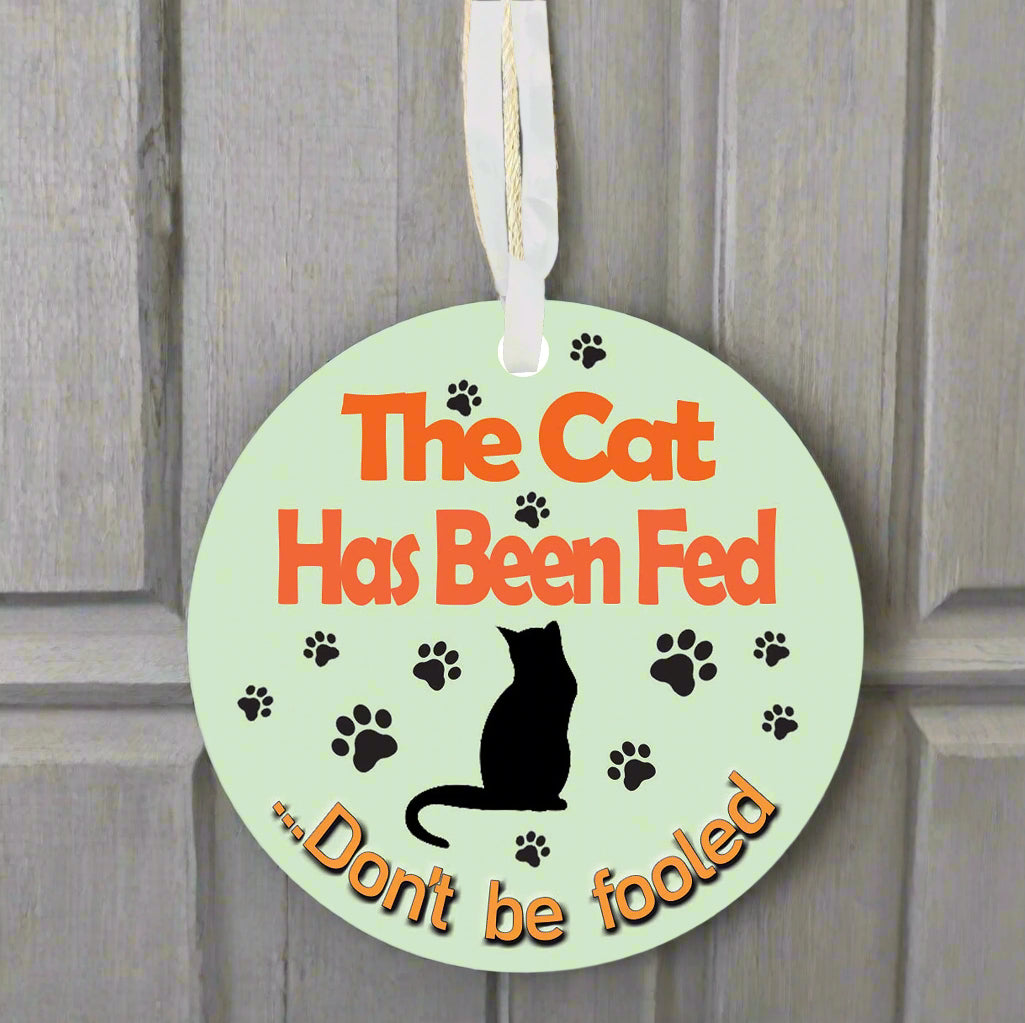 Round green sign with text 'The Cat Has Been Fed' and a black cat silhouette on a white background.